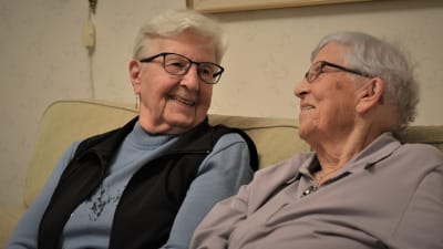Två äldre kvinnor ser på varandra och ler.