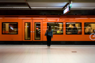 En människa står på perrongen framför en metro i rörelse.