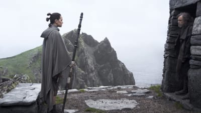Rey (Daisy Ridley) står utanför ett stenhus och ser på Luke Skywalker (Mark Hamill) som står i dörröppningen och inte vill umgås.