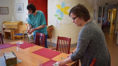 Två personer lägger ut bestick i matsalen i äldreboendet solglimten.