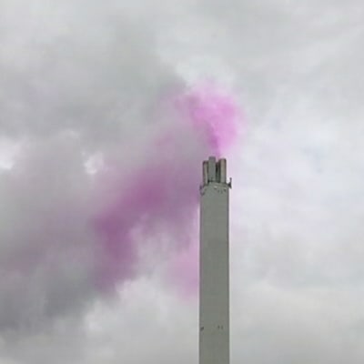 Vaaleanpunaista savua tulee tehtaan piipusta.