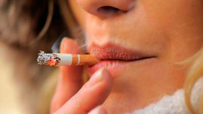 Närbild av en kvinna som röker. I bild syns endast hennes läppar, tobaken och hennes fingrar runt tobaken.