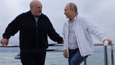 Aleksandr Lukasjenko och Vladimir Putin står på en båt och ler mot varandra. 