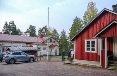 En gård med två trähus, ett rött och ett gult. En bil står parkerad vid en flaggstång.