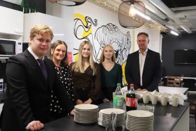 Fem personer står invid ett dukat bord och ser in i kameran. 