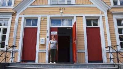 En person står på en trappa framför ett gult hus.