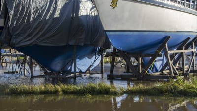Två stora båtar står förvarade på land på varsin ställning. Marken är täckt av vatten.