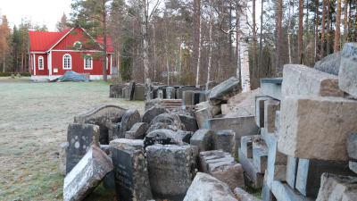 Gravstenar som plockats bort, står i utkanten av Åsändans begravningsplan och det röda kapellet í bakgrunden