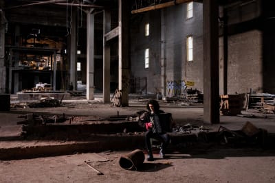 Nuori mies istuu romuja täynnä olevassa hylätyssä varastorakennuksessa soittamassa harmonikkaa.