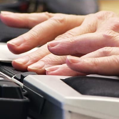Henkilö kirjoittaa tietokoneella, lähikuva käsistä näppäimistöllä.