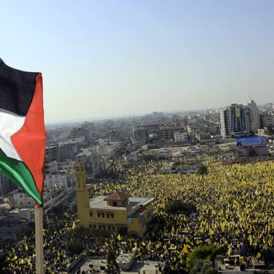 Aukio täynnä ihmisiä Palestiinan lippu edessä.