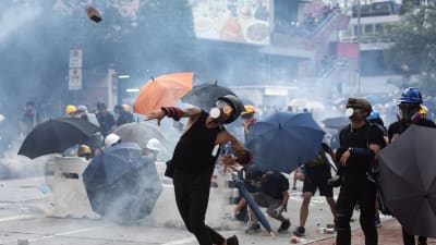 Demonstrant i Hongkong svarar på polisens tårgas med att kasta en tegelsten.