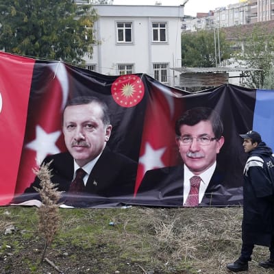 Asuinalueella naruun ripustettu vaalimainos, jossa Erdoğanin ja Davutoğlun kuvien lisäksi Turkin ja AKP-puolueen lippu. Edessä seisoo poliisi. 