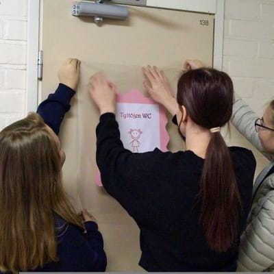 Oppilaat kiinnittämässä merkkiä koulun vessan oveen.