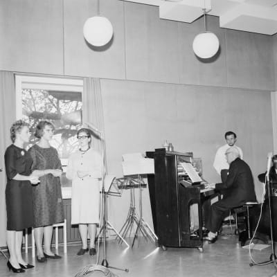 En man spelar på piano och tre kvinnor sjunger.