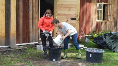 Ingrid Henriksson och Eva Godenhielm-Vuori blandar ihop massan för lerklining ute på gården.