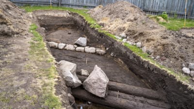 Stockar och stenar i ett schakt som arkeologer gräver ut. De visar att det funnits hus från 1700-talet och 1800-talet på platsen.