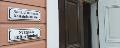Skyltar med texten Nostalgi-museum, Nostalgia-museo och Svenska kulturfonden vid en dörr som står öppen.