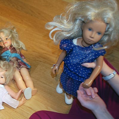 Kuvassa nukkeja lattialla ja tyttö leikkimässä niillä