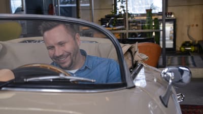 Roni Collin sitter i en gammala beige öppen Porsche. Han ler. Bilen är inomhus vid hans kontor.
