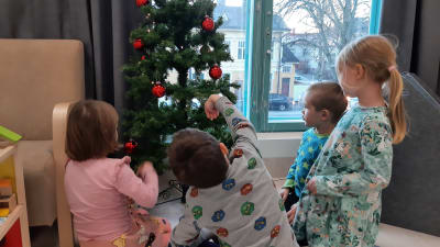 Fyra barn tittar på en julgran med röda bollar.
