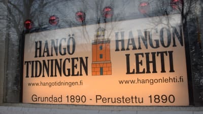 Ett skyltfönster som tillhör Hangötidningen. Där finns tydliga skyltar som visar att tidningsredaktionen finns inne i just det stenhuset.