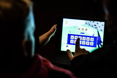 Barn sitter med pekplatta i handen och spelar ett spel