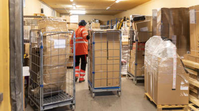 En man drar en kärra med paket som hämtats till ett paketombud. Där finns många andra kärror med paket.