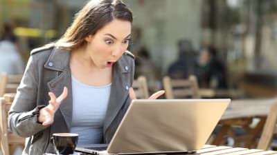 Nainen katsoo hämmentyneenä kannettavan tietokoneen näyttöä ulkokahvilan pöydässä.