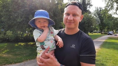 Man med lippis och en bebis i solhatt.