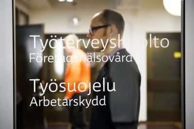 Två män bakom en dörr med glasruta, texter om företagshälsovård och arbetarskydd.