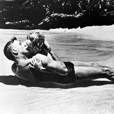 Mies (Burt Lancaster) ja nainen (Deborah Kerr) uima-asuissa suutelevat intohimoisesti rantahiekassa maaten.