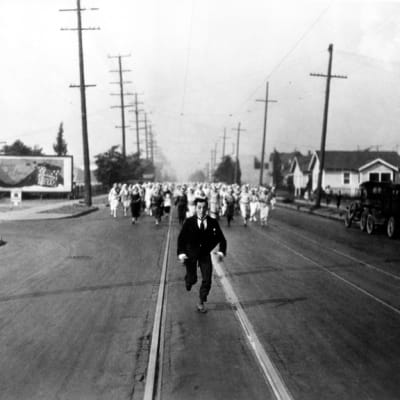 Mies (Buster Keaton) juoksee kadulla pakoon kymmeniä morsiameksi pukeutuneita naisia.