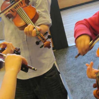 Kolme nuorta soittajaa soittaa viulua.