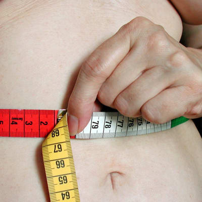 Lihava nainen pitelee mittanauhaa vatsansa ympäri.