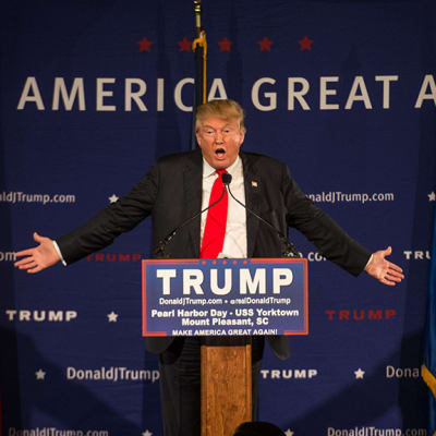 Donald Trump kädet levällään puhujankorokkeella.