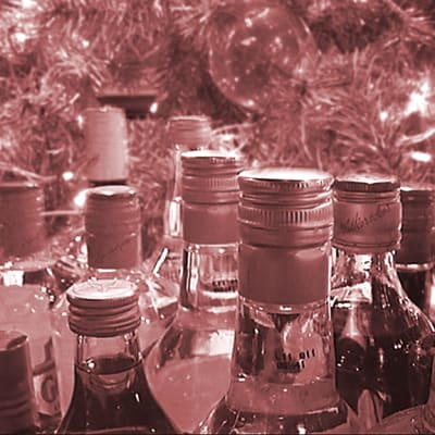 Vaaleanpunaiseksi sävytetty kuva alkoholipulloista kuusenoksien ja jouluvalojen keskellä.