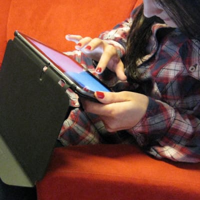 Nuori nainen selailee tablettitietokonetta sohvalla.