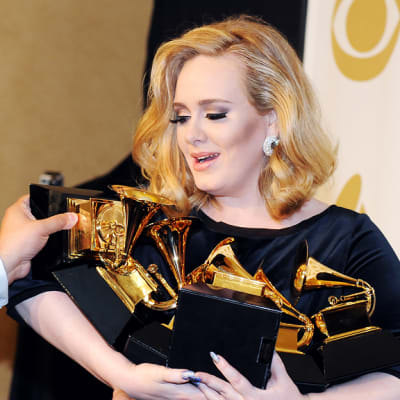 Avustaja asettelee Grammy-palkintoja Adelen syliin.