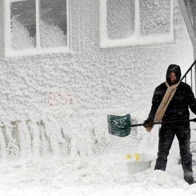 Mies lapioi lunta pois talon portailta Massachusettsin Winthropissa.