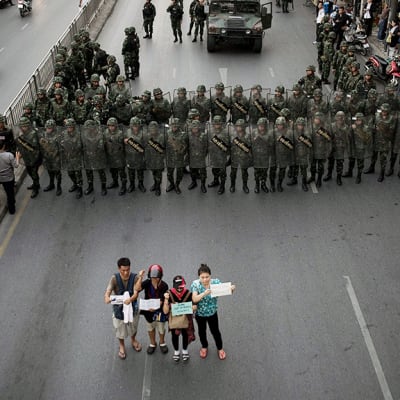 Neljä ihmistä osoittaa mieltään sotilaiden edessä Bangkokissa.