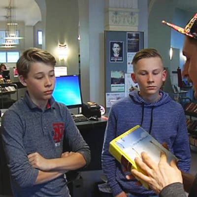 Mies esittelee kirjaa kahdelle pojalle kirjastossa.