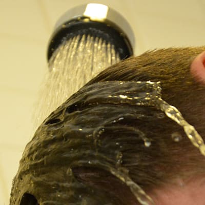 Mies kastelee suihkulla hiuksiaan.