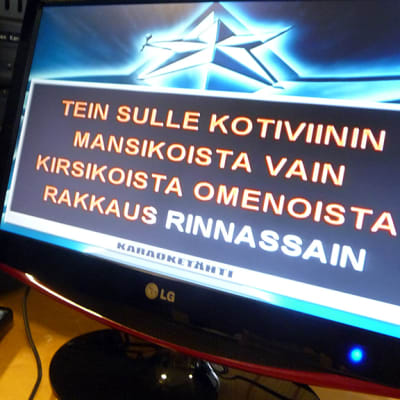 Lähikuvassa karaokelaitteen näytöllä kotiviini-kappaleen sanoja.
