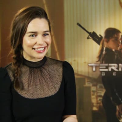 Hymyilevä näyttelijä Emilia Clarke Terminator Genisys -elokuvajulisteen edellä.