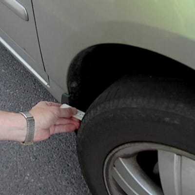 Poliisi mittaa auton renkaan kulutuspintaa.