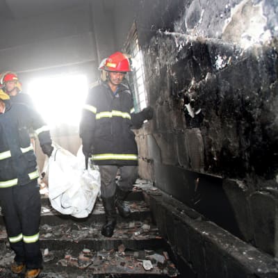Pelastustyöntekijät kantavat ruumista ulos palaneesta tehtaasta Bangladeshissa. 