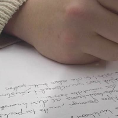Kuvassa lähikuva kirjoittavasta kädestä ja tekstistä
