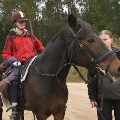 Ratsastusterapeutti auttaa hevosen selässä olevaa kuntoutettavaa