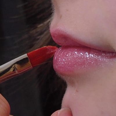 Meikkitaiteilija levittää huulikiiltoa tytön huulille